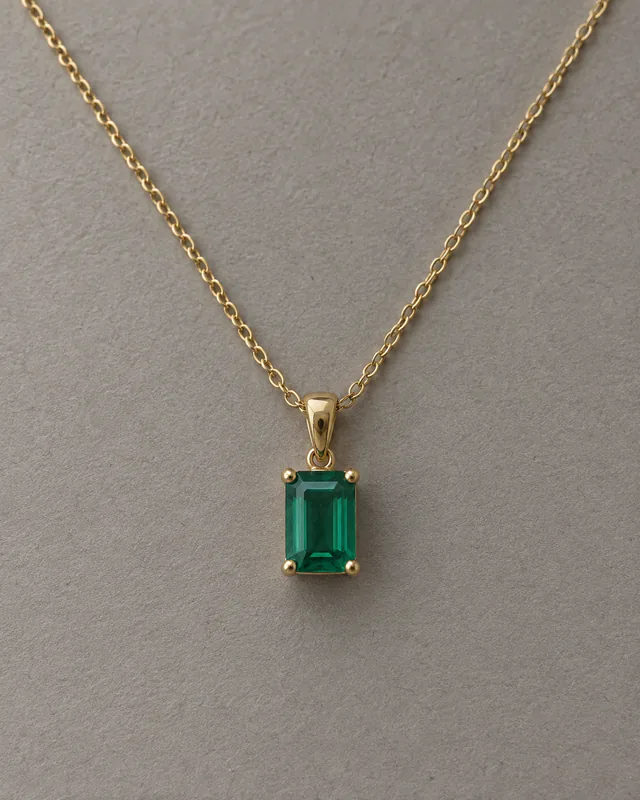 A rectangular emerald pendant necklace photographed on gray paper